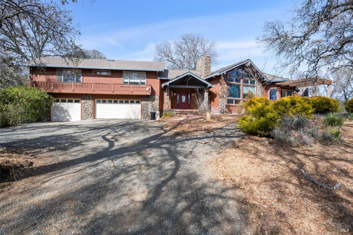 A large two-story house with stone and wood elements, featuring a three-car garage and a sloped driveway.