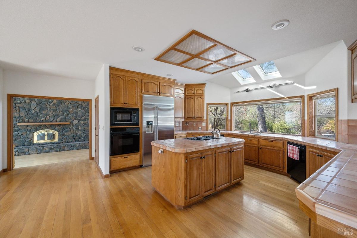 kitchen with a warm and natural aesthetic, featuring wooden cabinetry, an island with a cooktop, and tile countertops.