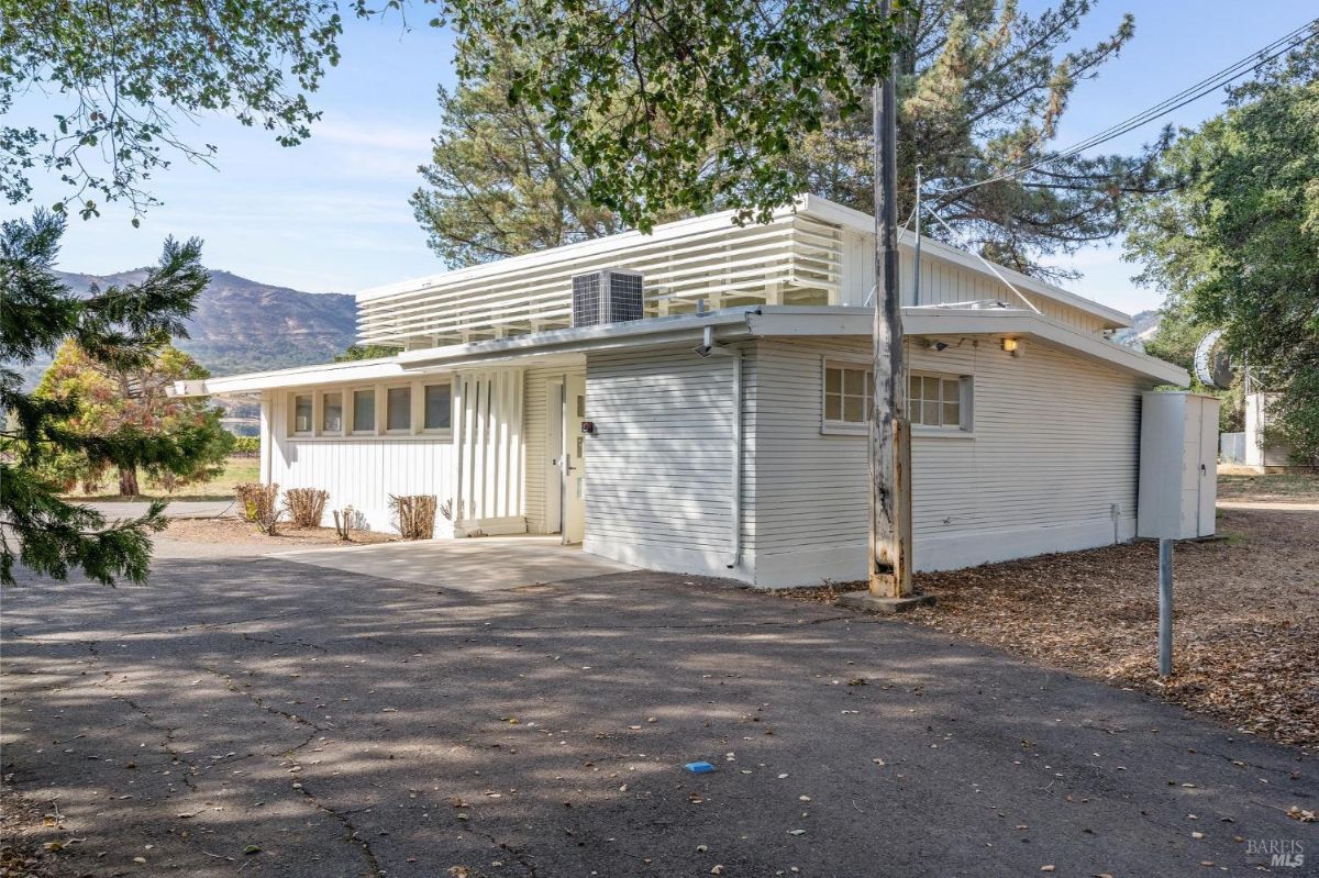  A single-story white building with horizontal siding, large windows, and a paved driveway.