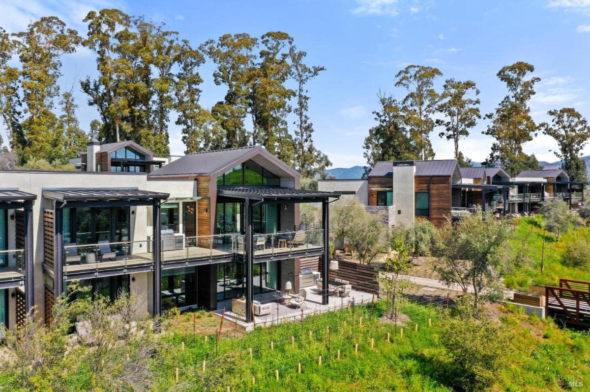 A modern multi-story home with glass and wood exterior elements surrounded by trees.