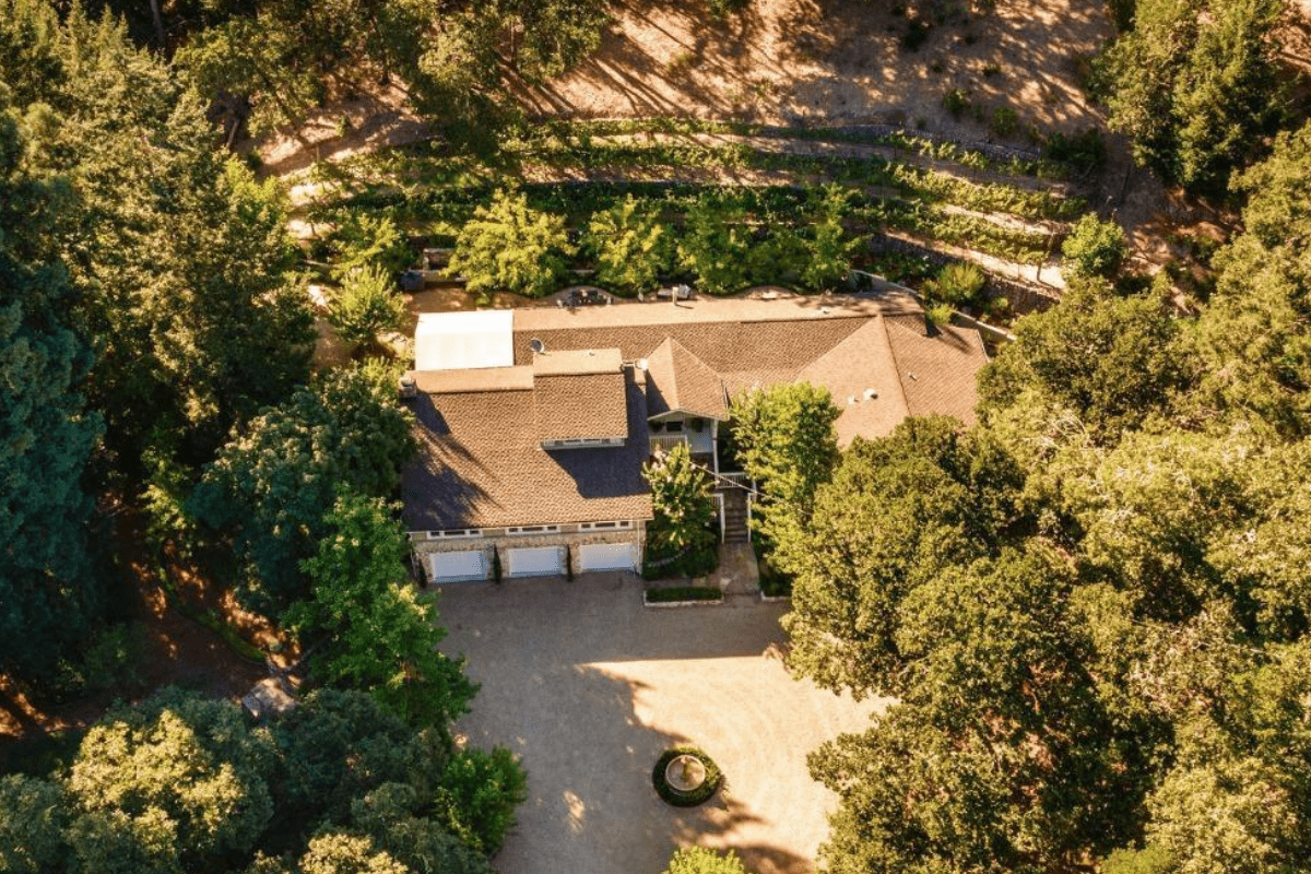 Aerial view of a large house surrounded by trees and landscaped gardens.