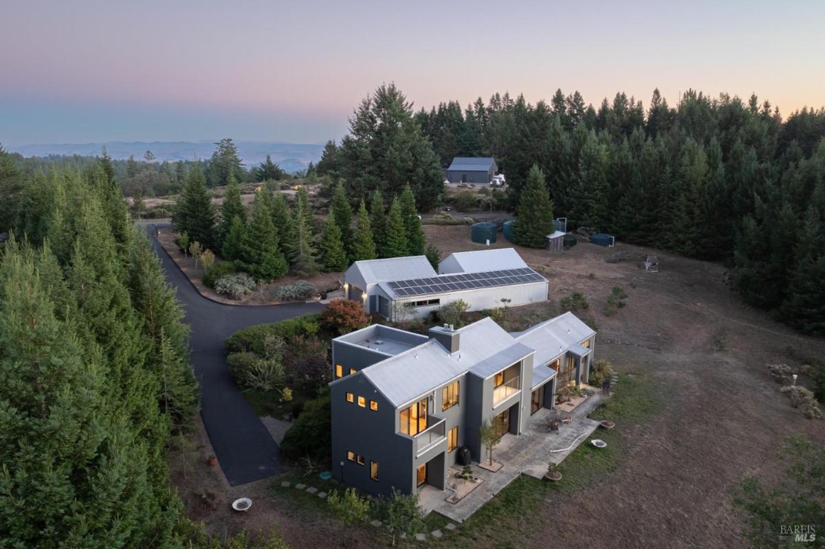 A modern home surrounded by trees with a solar panel installation and paved driveway.