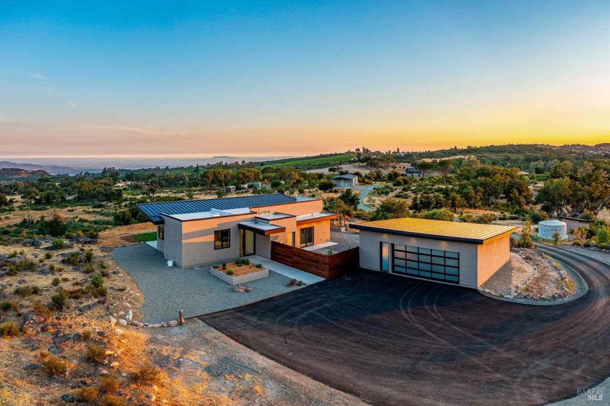 A modern home with a flat roof and a detached garage surrounded by open countryside.