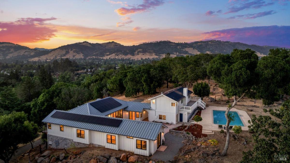 A white home with solar panels and a pool, set against a hillside landscape.