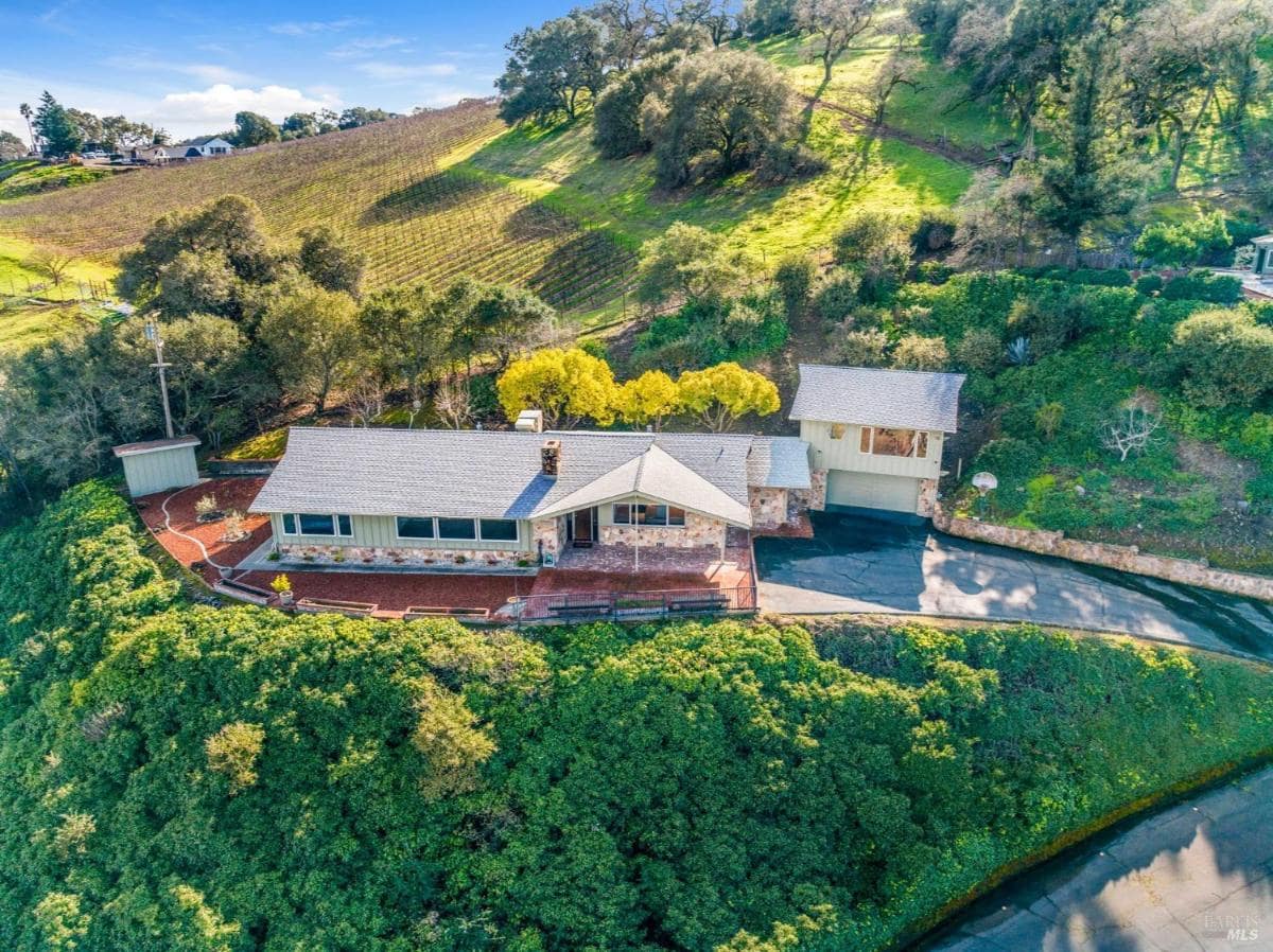 Aerial view of a house nestled in a hillside with vineyards.