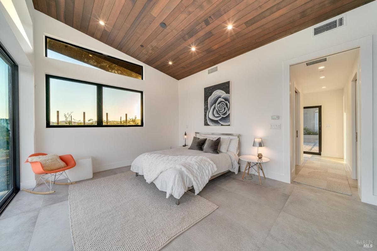 A bedroom with a wood-paneled ceiling, large windows, and minimalist decor.