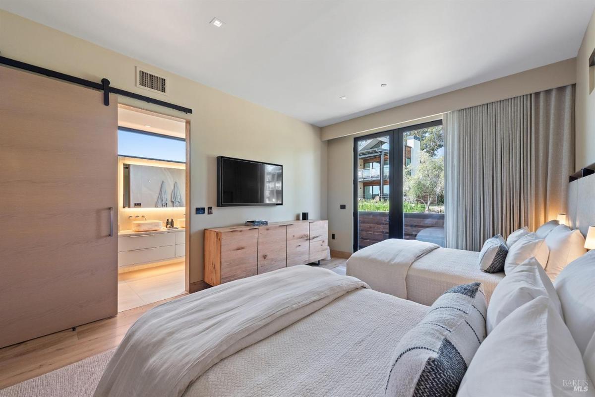 A bedroom with twin beds, a wooden dresser, and a sliding door opening to a bathroom.