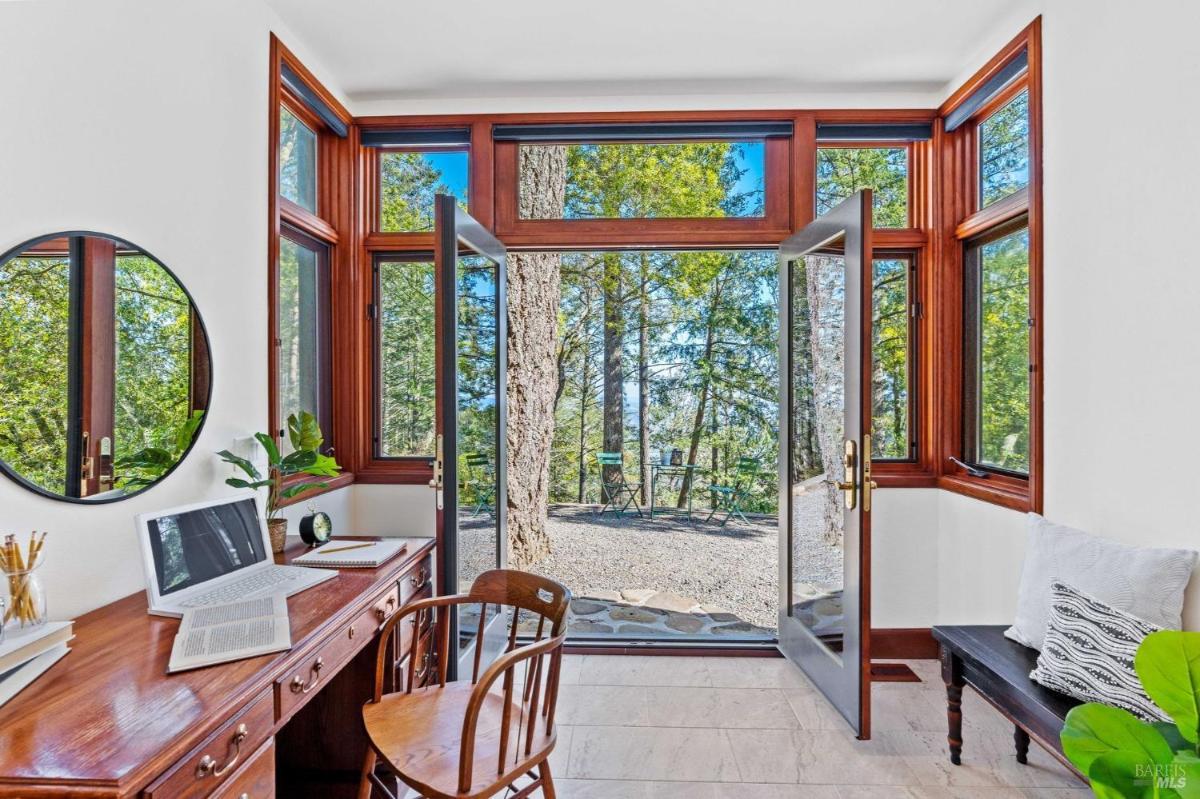 Study with desk and double doors opening to a patio with trees outside.