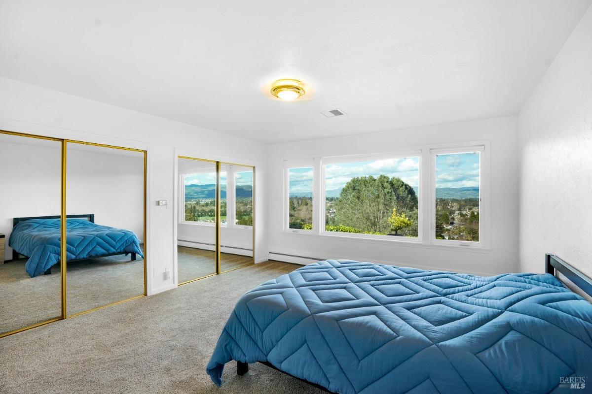 Bedroom with mirrored closets and large windows showcasing a landscape view.