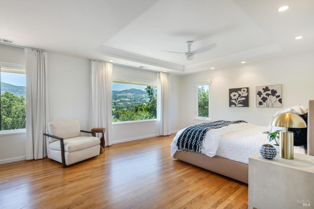 A bedroom with hardwood floors and large windows offering outdoor views.