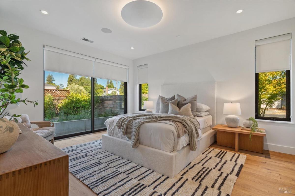 Bedroom with large windows, bed, and wooden furniture.