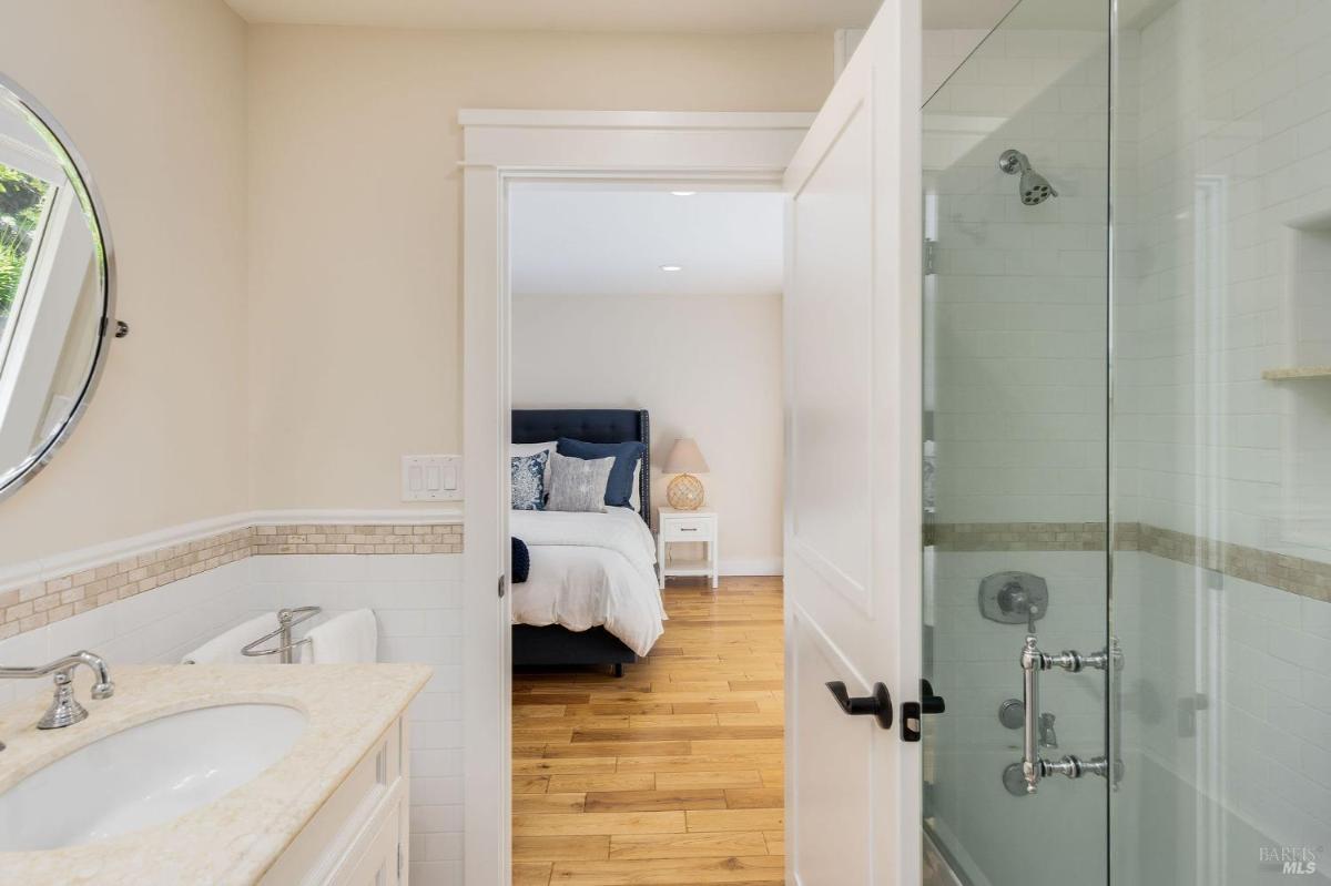 A view of a bathroom with a glass shower and a doorway leading to a bedroom.

