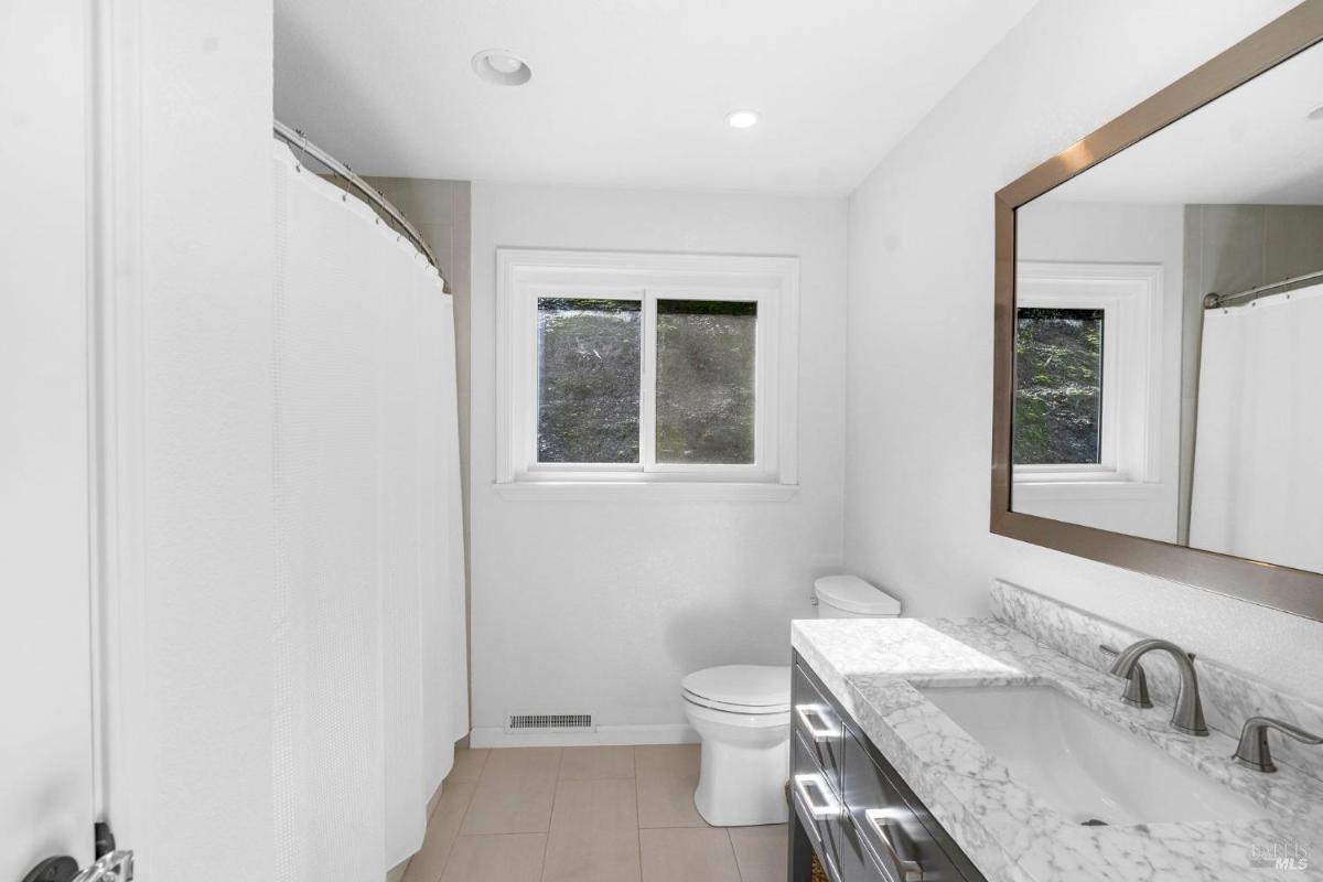 Bathroom with a marble countertop, shower, and a window.