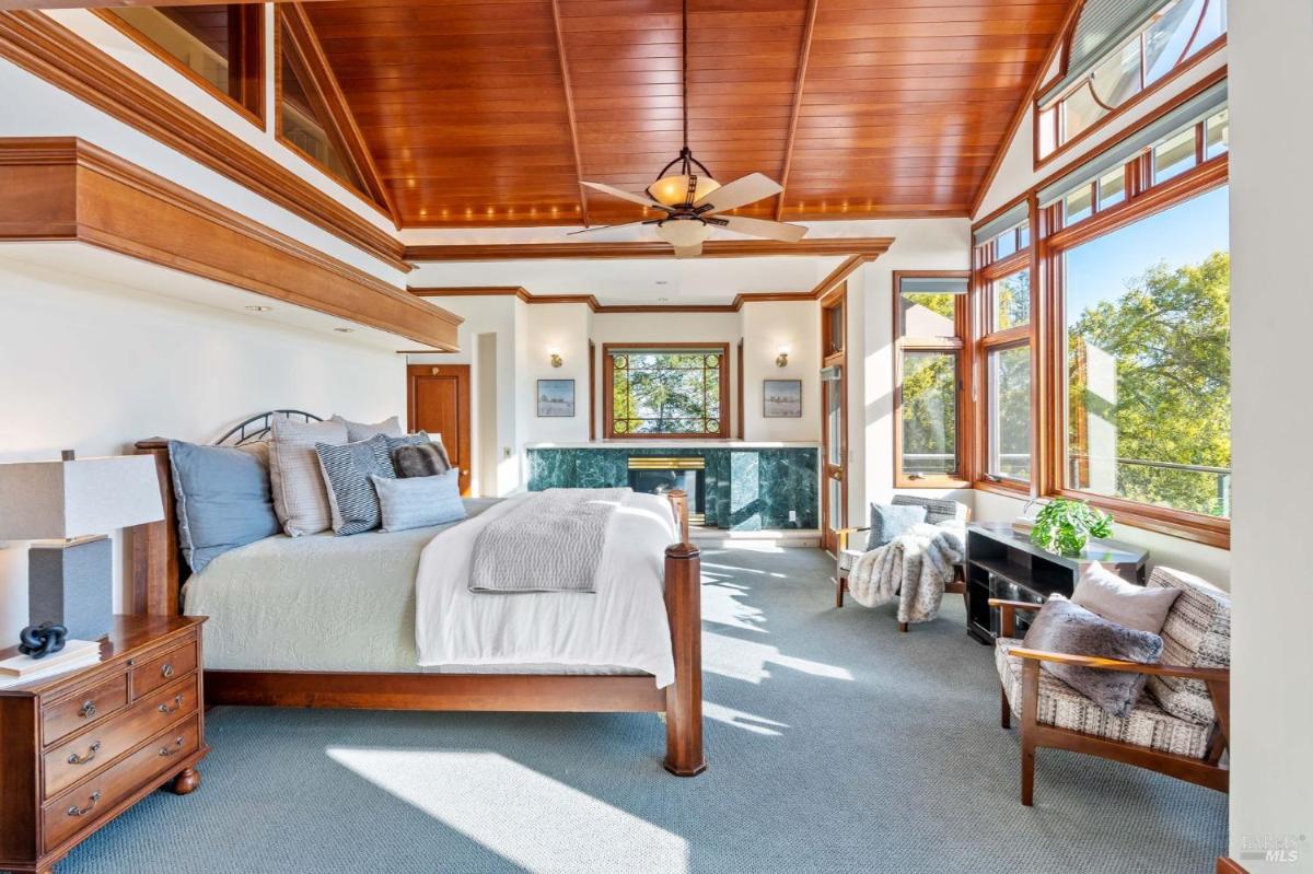 Spacious bedroom with large windows, wooden ceiling, and a fireplace.