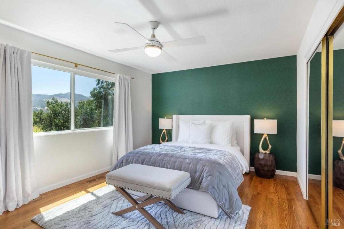 A bedroom with a green accent wall, hardwood floors, and a window with outdoor views.