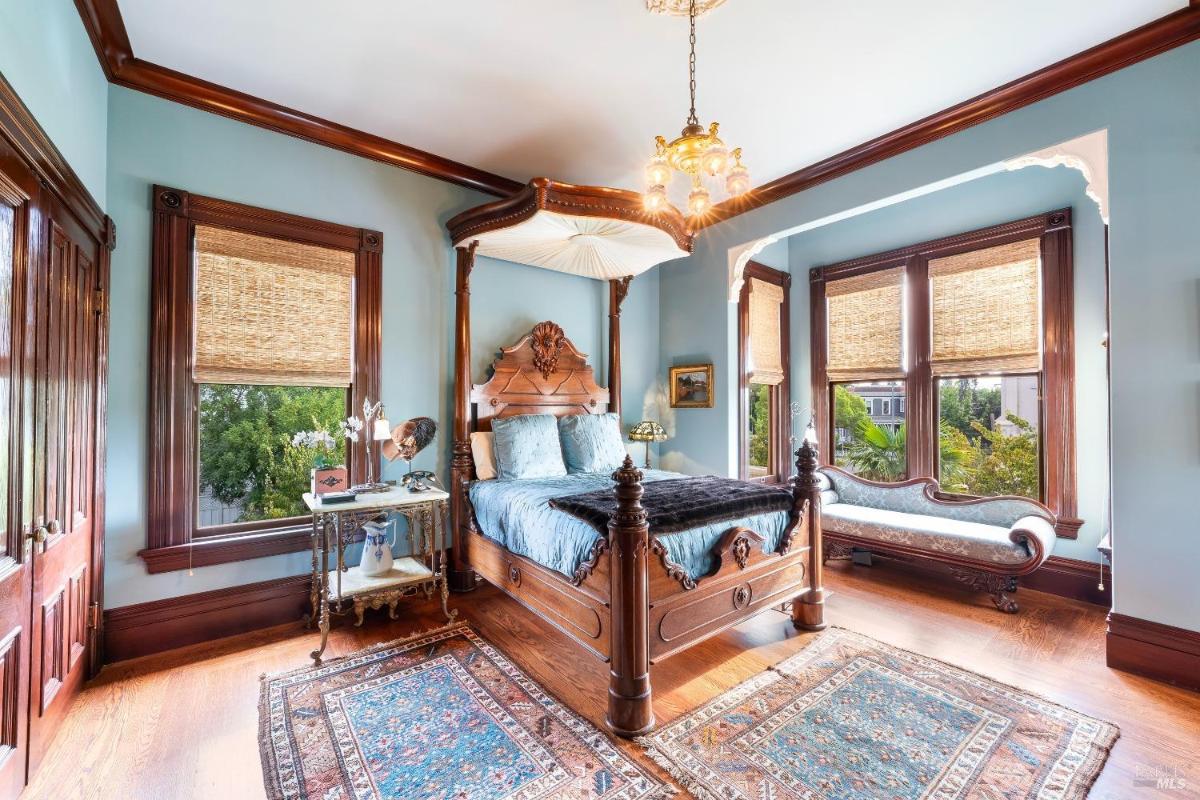 A bedroom with a canopy bed and wood-trimmed windows.