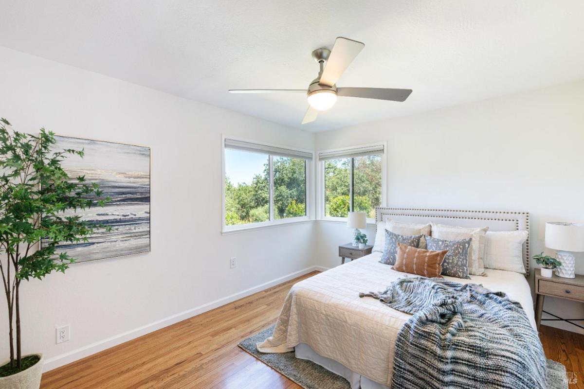 A bedroom with corner windows, a ceiling fan, and hardwood floors.