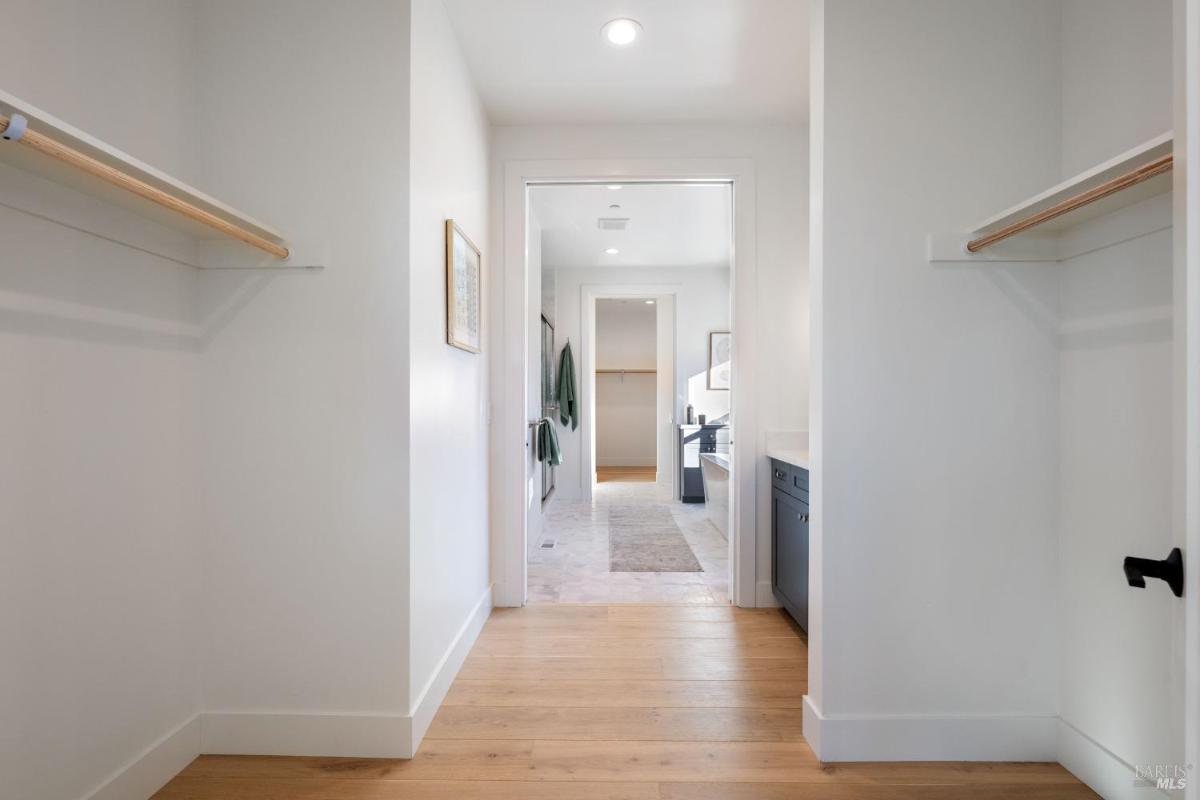 Walk-in closet with hanging rods and a view into the bathroom.