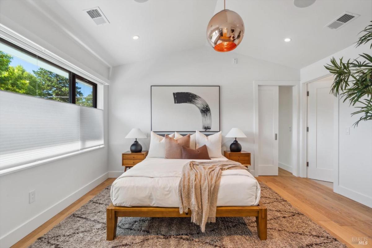 Bedroom with abstract wall art, a bed with white bedding, wooden frame, and side tables under an abstract art piece.