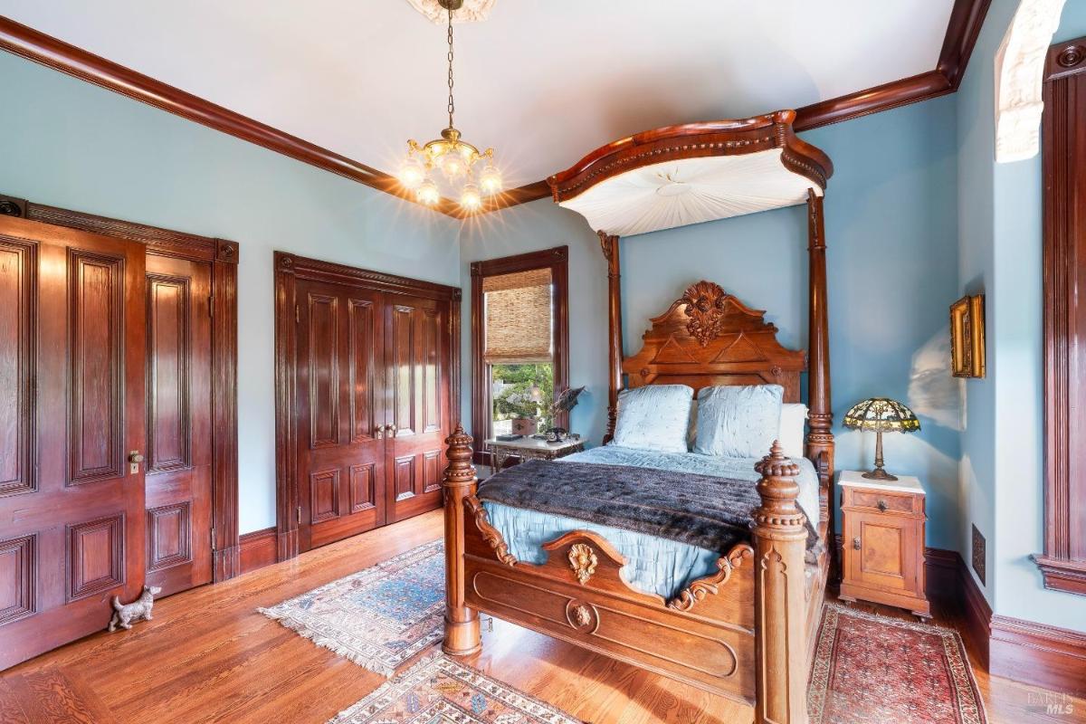 The same bedroom from a different angle, showing a canopy bed and wooden double doors.