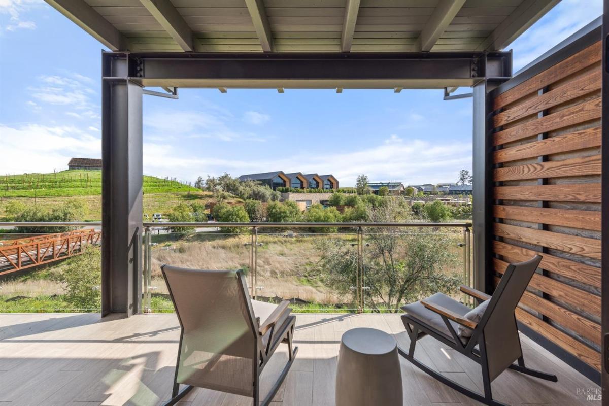 A balcony with rocking chairs, a small table, and views of a bridge and greenery.