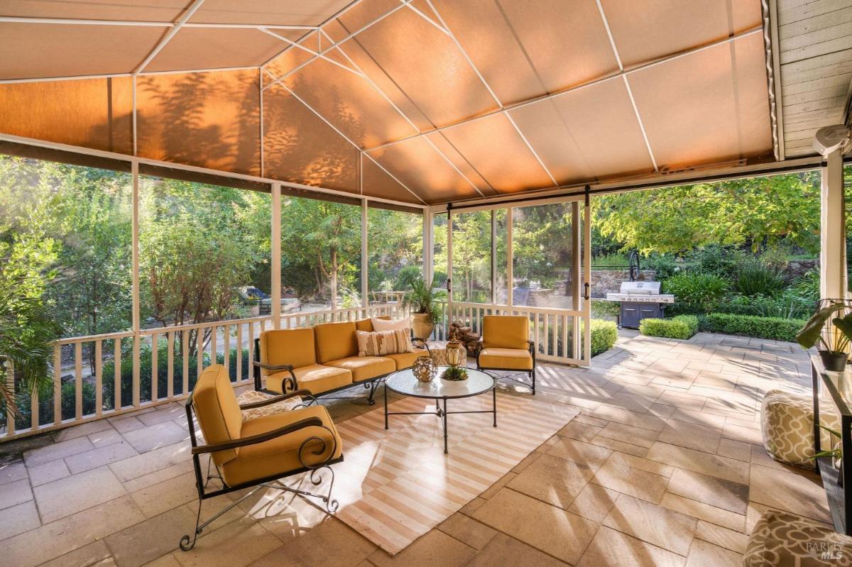 A screened porch with seating, a coffee table, and sunlight filtering through the canopy.

