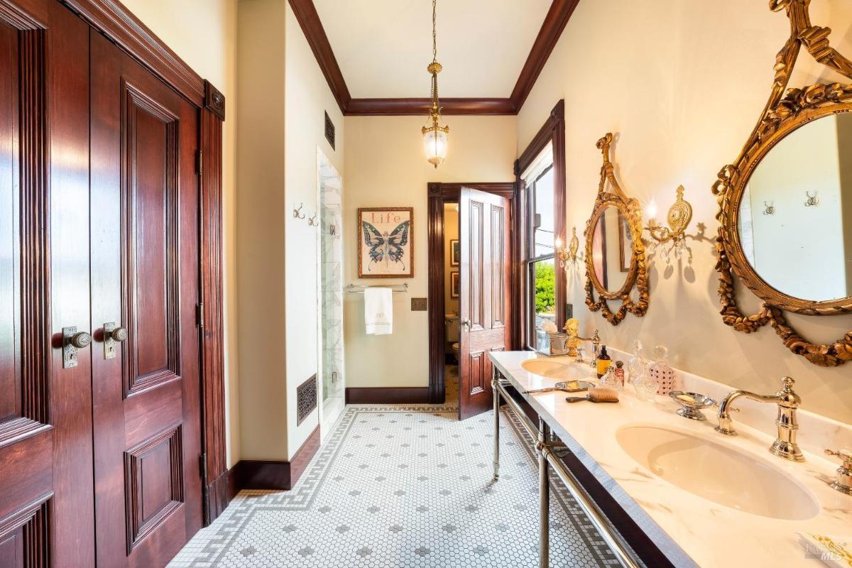 A bathroom with dual sinks, ornate mirrors, and tiled flooring.