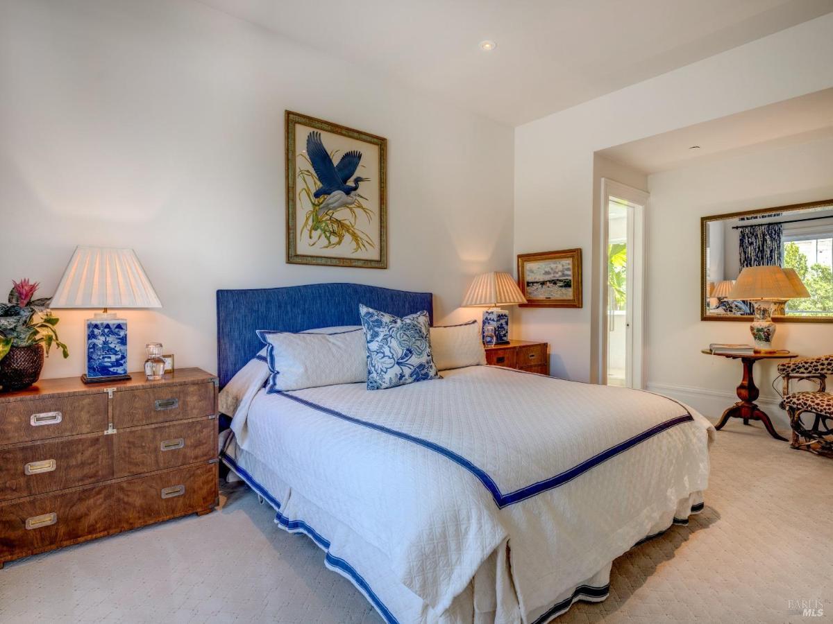 A bedroom with a blue upholstered bed, wooden nightstands, and a framed bird illustration.