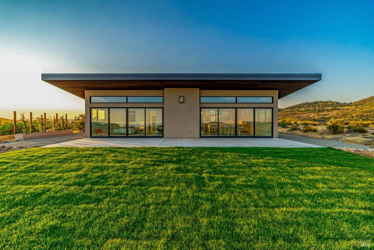 A rear view of a modern home with glass doors opening to a green lawn.