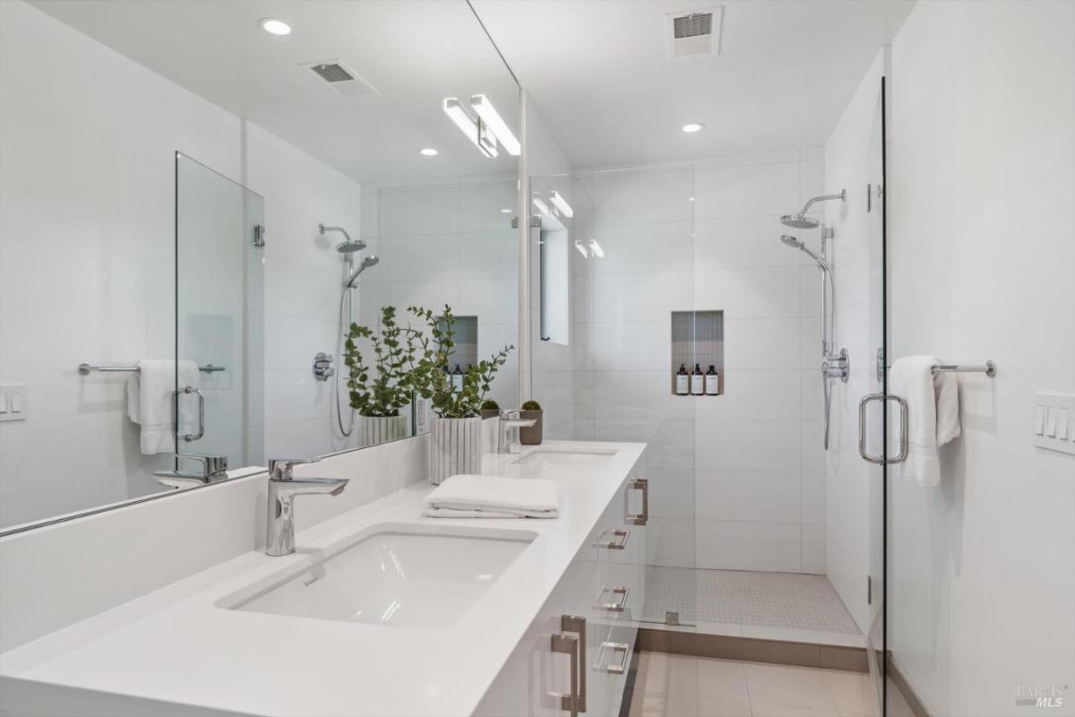 Bathroom with green accents, white double vanity bathroom with a glass shower and a green potted plant on the counter.