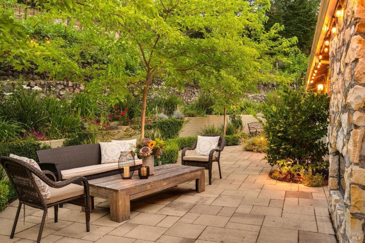 A seating area with a sofa and coffee table is located in a garden with plants and lighting.