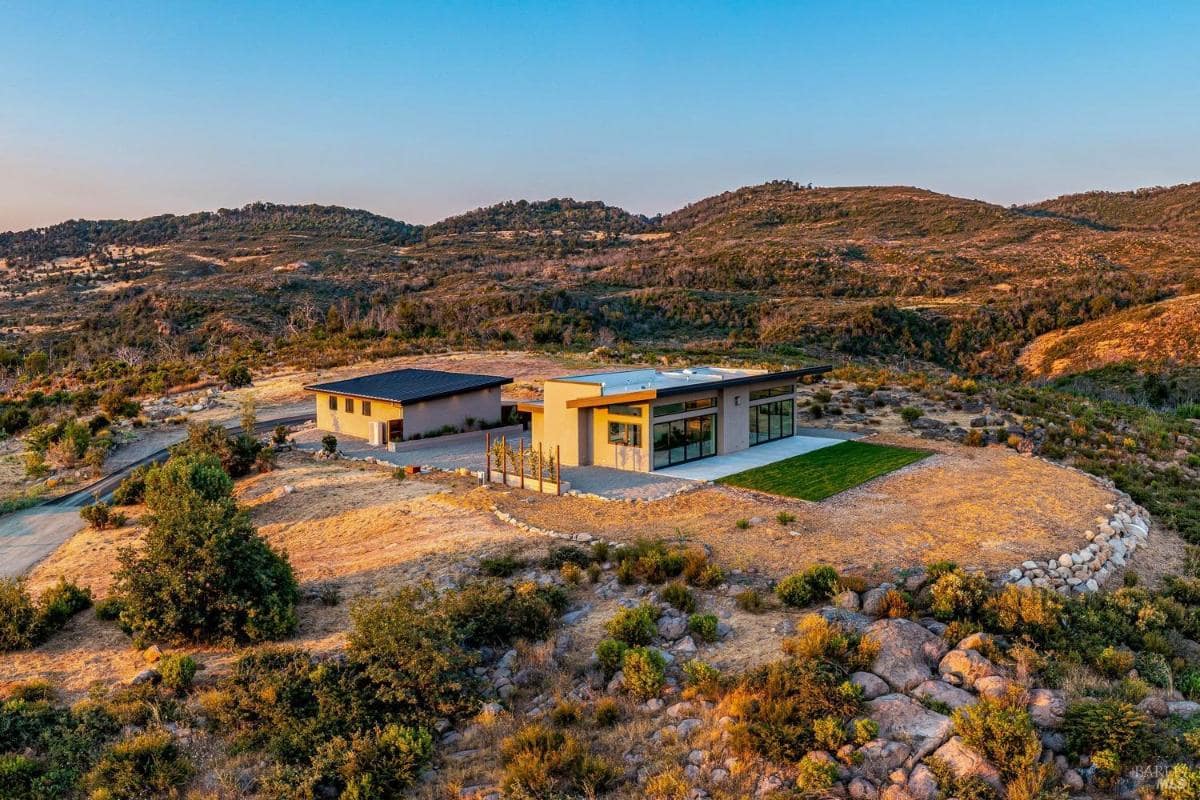 An aerial view of a modern home situated in a hilly landscape.