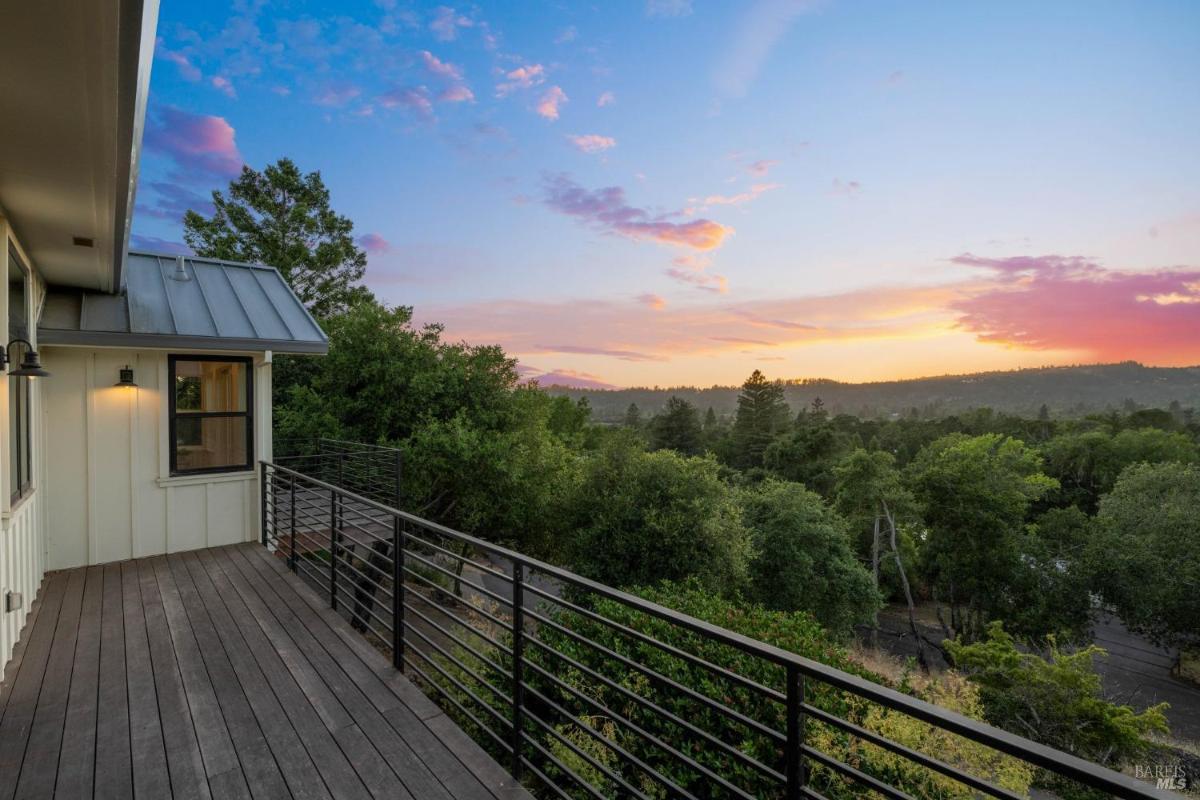 Balcony with a view of trees and a sunset in the distance.