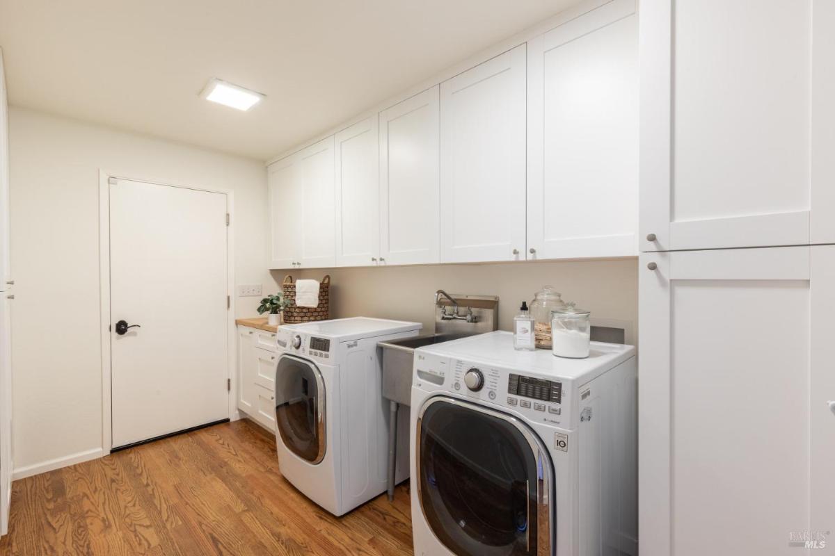 A laundry room with white cabinets, a sink, and front-loading washer and dryer.