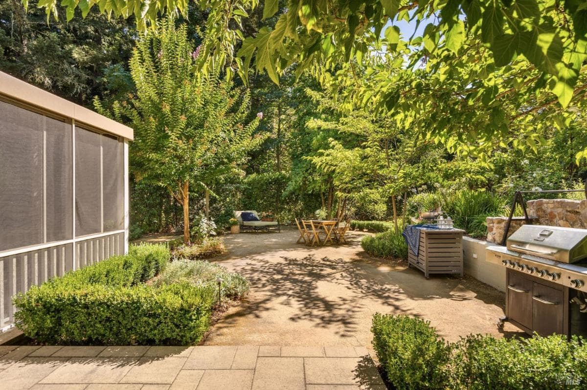 An outdoor space features a grill, seating area, and surrounding greenery.

