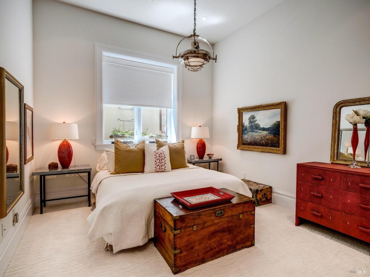 A bedroom with a white bed, red accents, and a wooden chest.