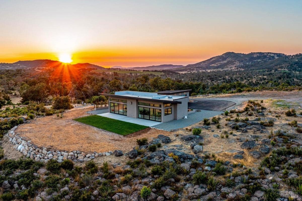 A sunset view of a modern home surrounded by open land.