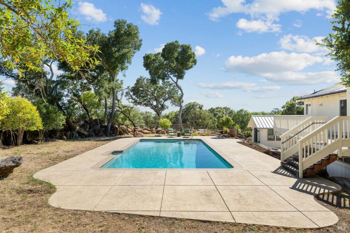 Outdoor pool surrounded by trees and a concrete deck.