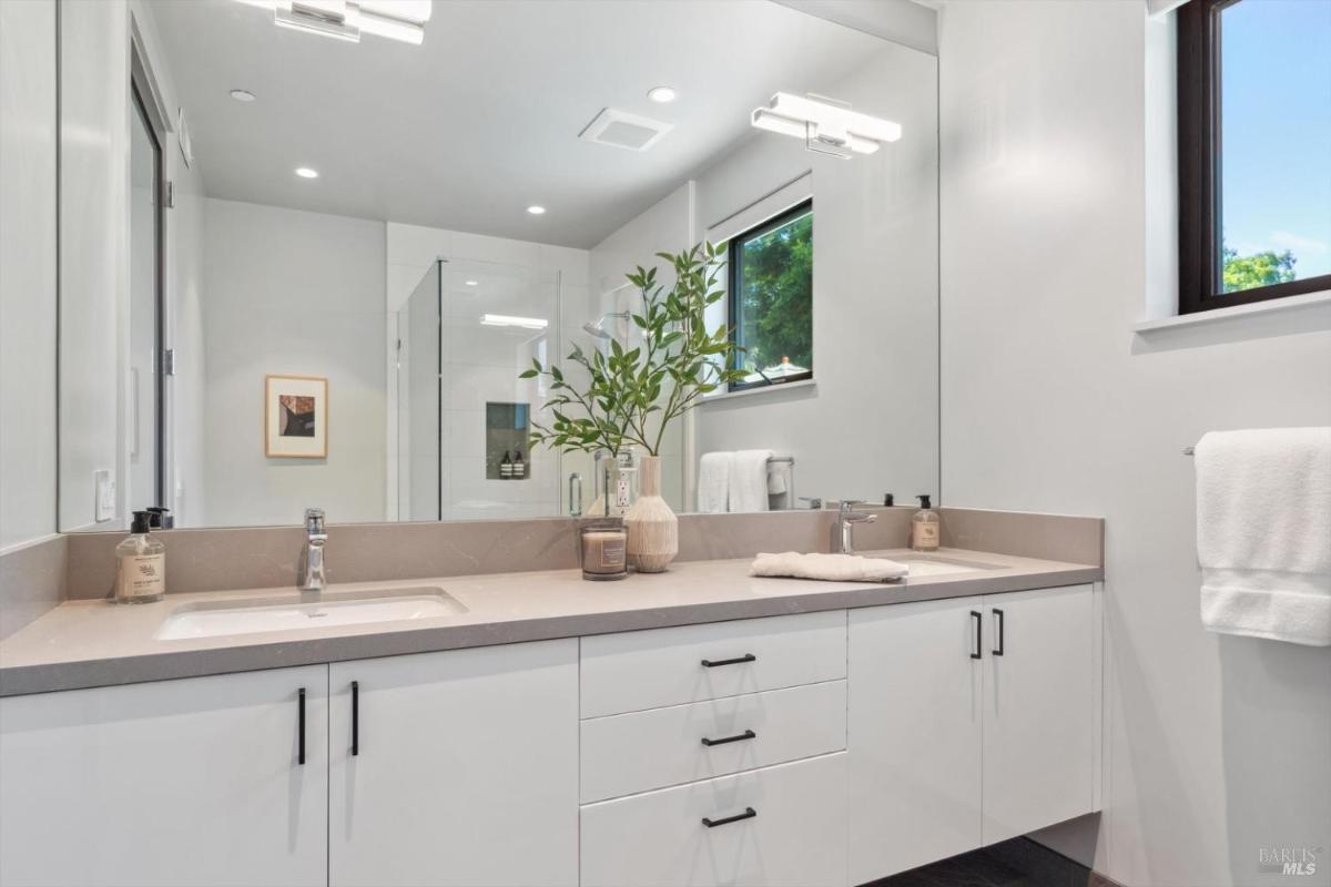 Bathroom with double vanity bathroom with a large mirror, a glass shower, and natural light from a window.