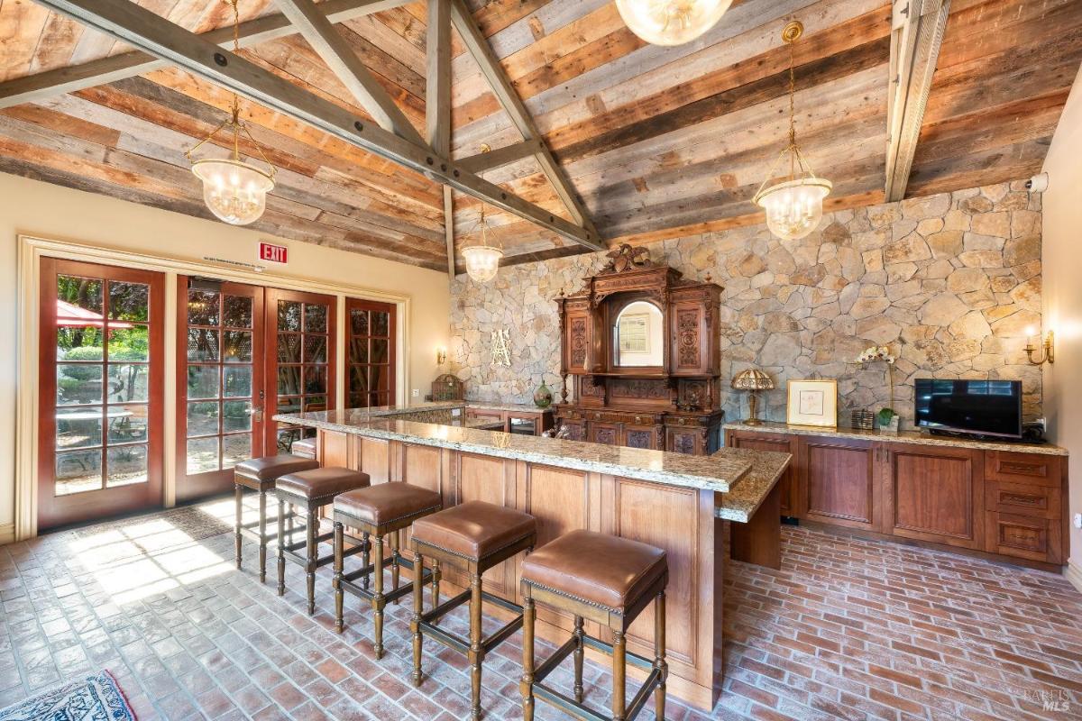 A bar area with brick flooring, wooden stools, and a stone accent wall.