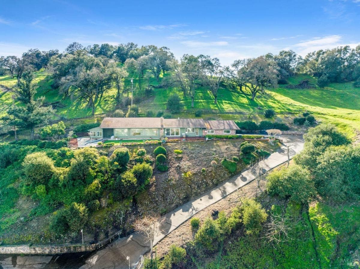 Hillside view of a house with a driveway and landscaping.