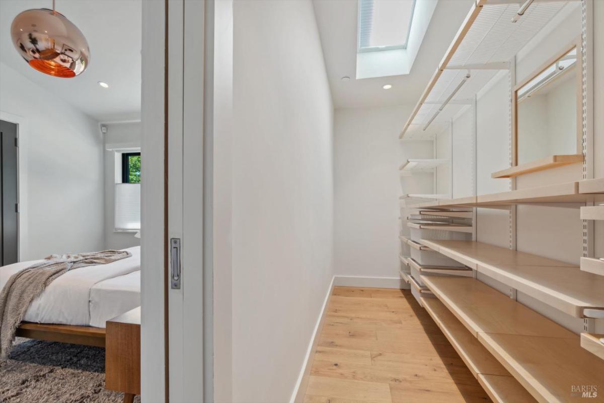 A walk-in closet with wooden shelving and drawers, illuminated by natural light.