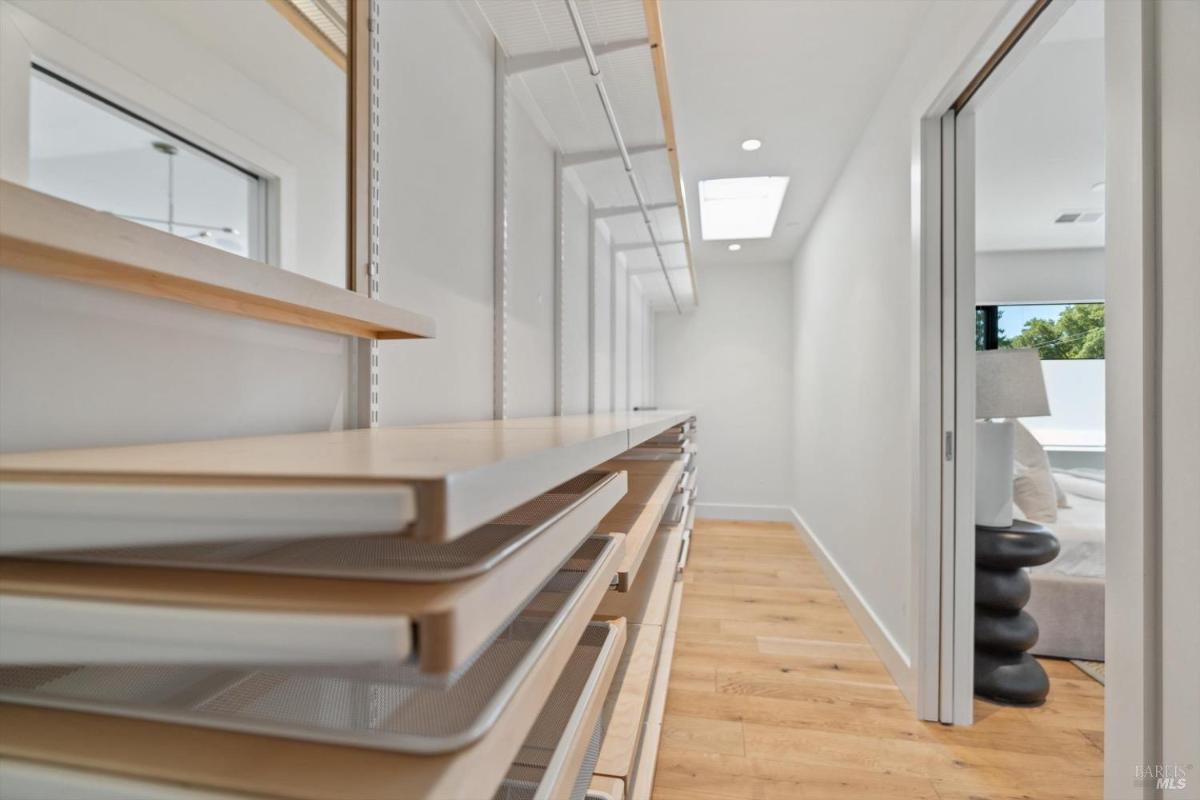 A long closet with open shelving, a skylight, and a view into a bedroom.