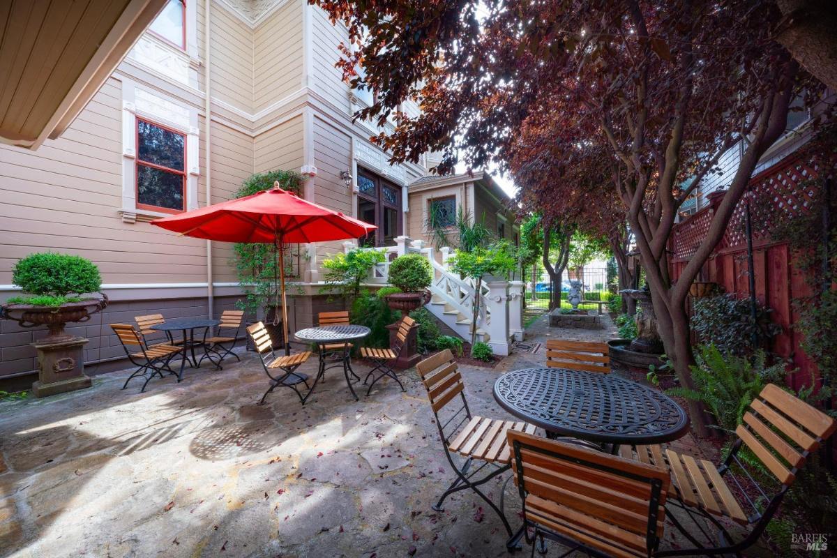 Backyard seating area with tables, chairs, and red umbrellas.