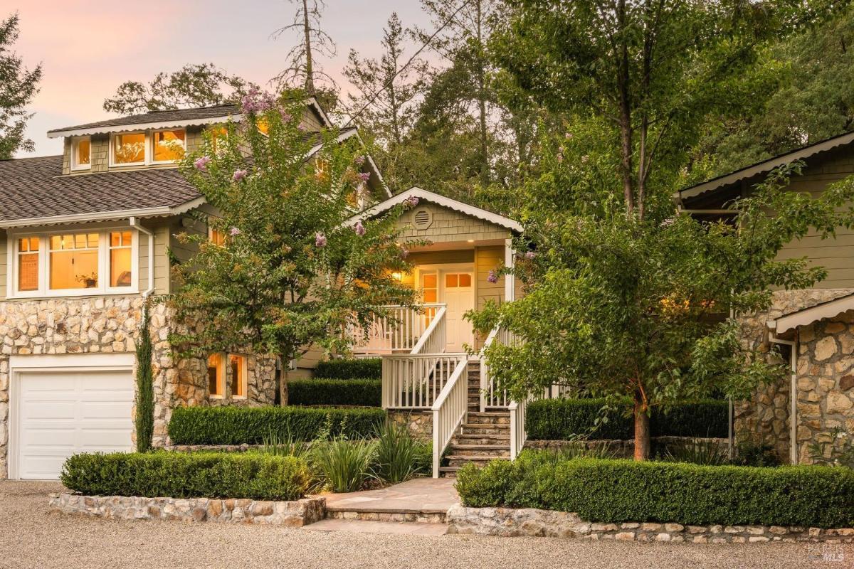 A house with a stone facade, front steps, and landscaped shrubs, with a garage on the left.

