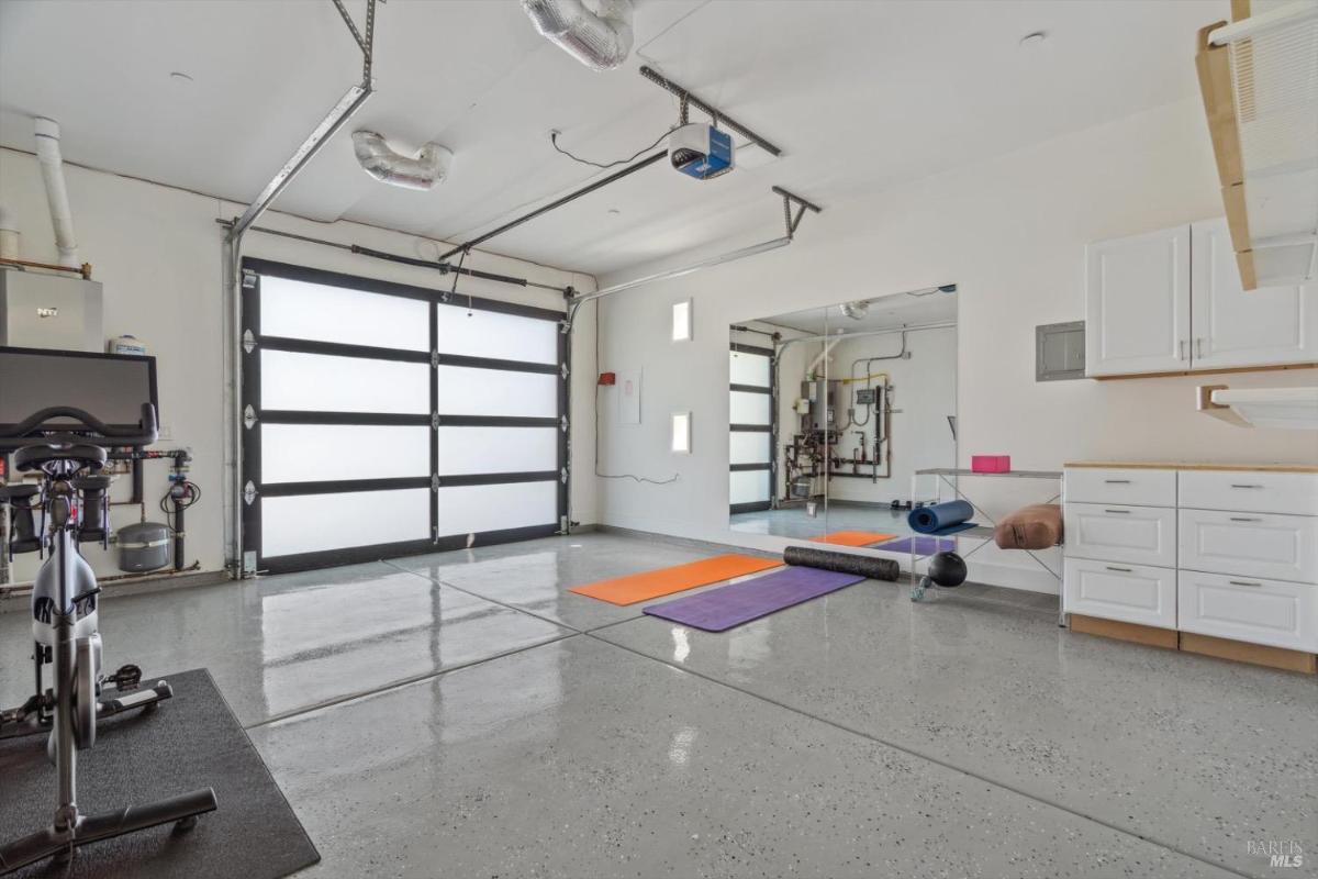 Garage space with fitness equipment and yoga mats, featuring polished concrete floors and wall cabinets.