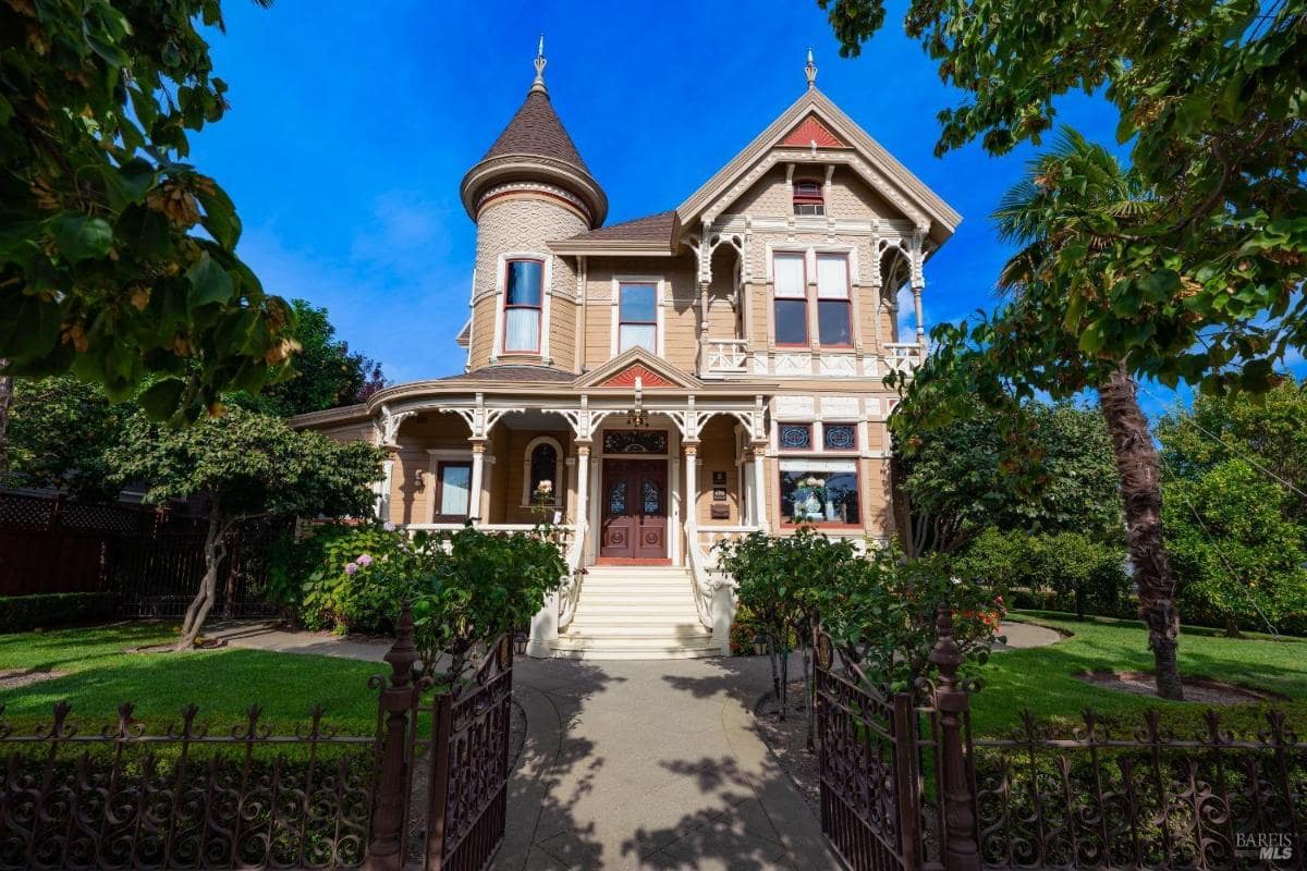 Front view of a Victorian-style house with a gated entrance and landscaped yard.