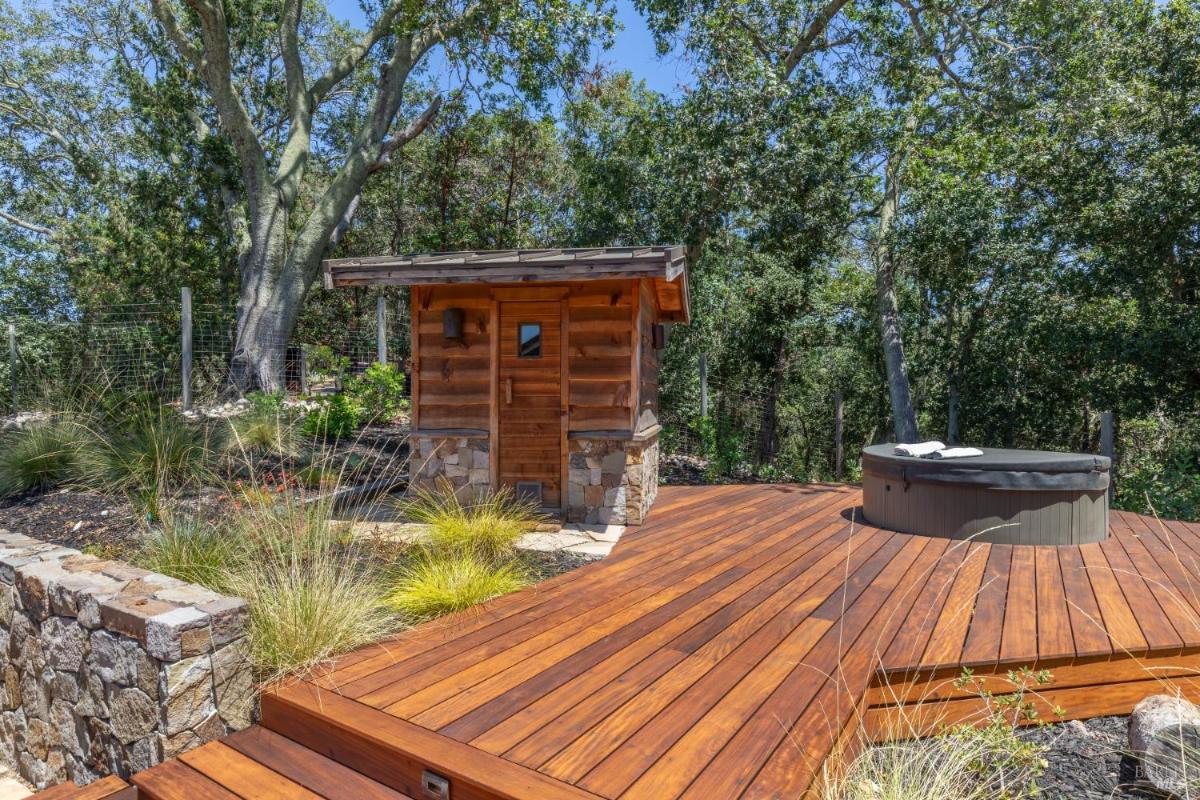 Wooden sauna and hot tub on a raised deck surrounded by trees.