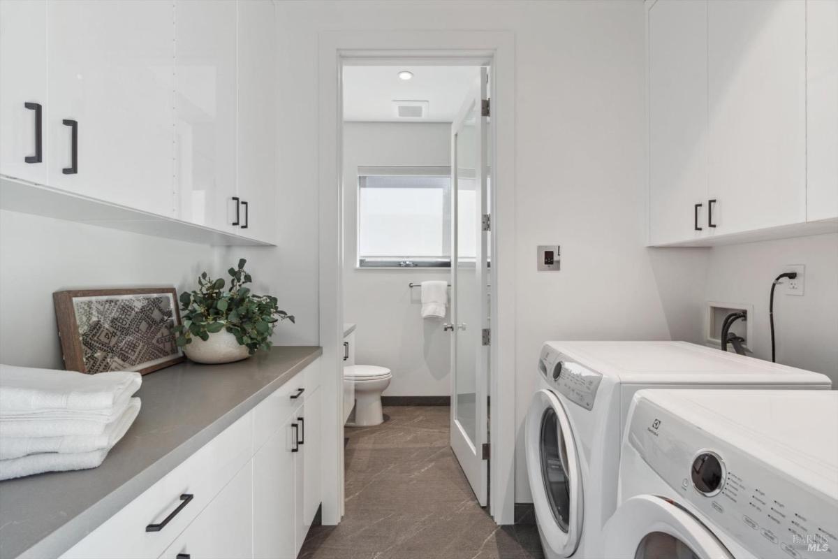 Laundry room with washer, dryer, countertop, and upper cabinets. A door leads to an adjacent bathroom.