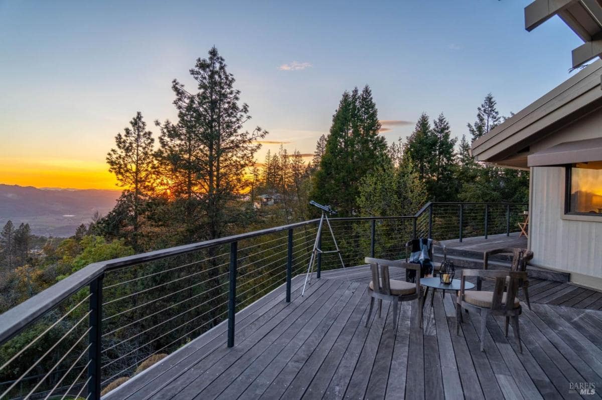 A deck with a telescope and chairs, set against a sunset view over the valley.